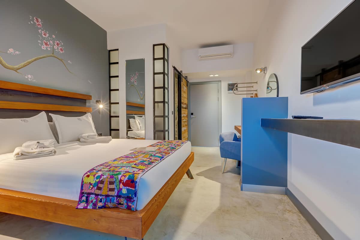 A modern hotel room with a wooden bed, a colorful blanket, a desk, and a blue chair.