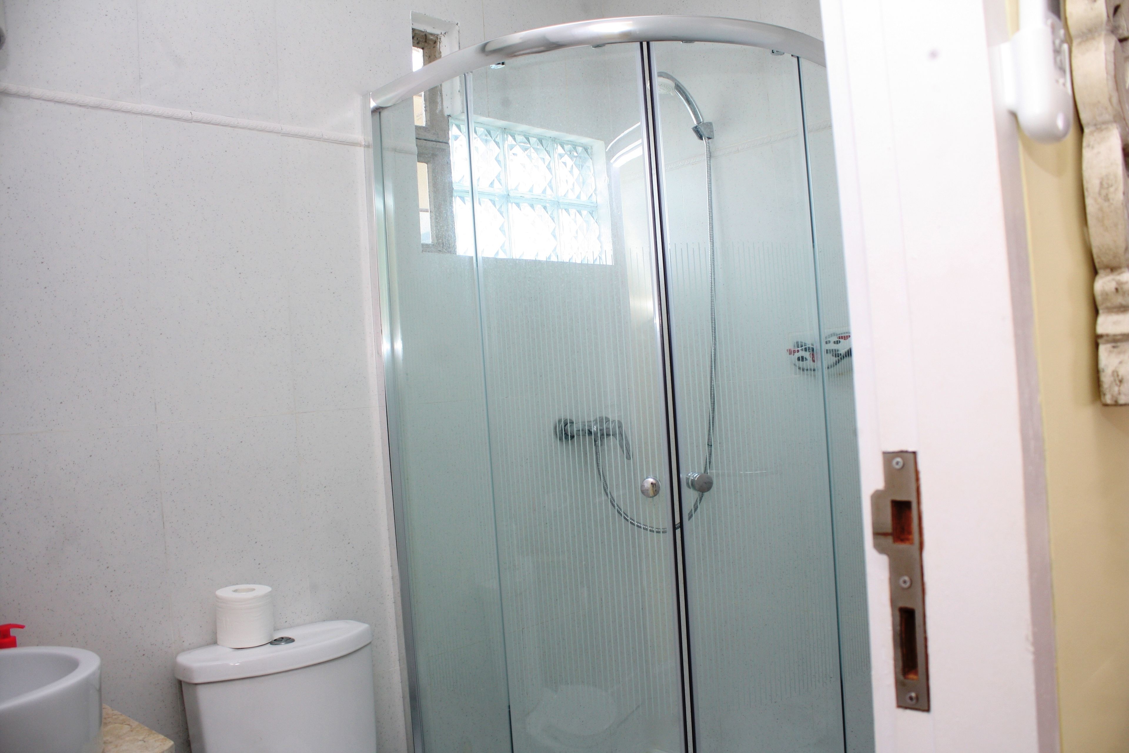 Une douche fermée par des parois de verre, avec des toilettes blanches et un distributeur de serviettes.