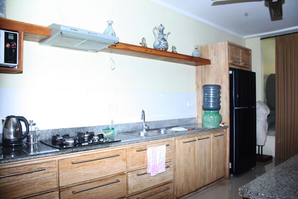 A kitchen with wooden cabinets, a stainless steel sink, a black refrigerator, and a water dispenser. - Villa Senja Semiyak (Seminyak)