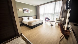 Quarto de hotel com uma cama grande, uma mesa, duas cadeiras e uma televisão.