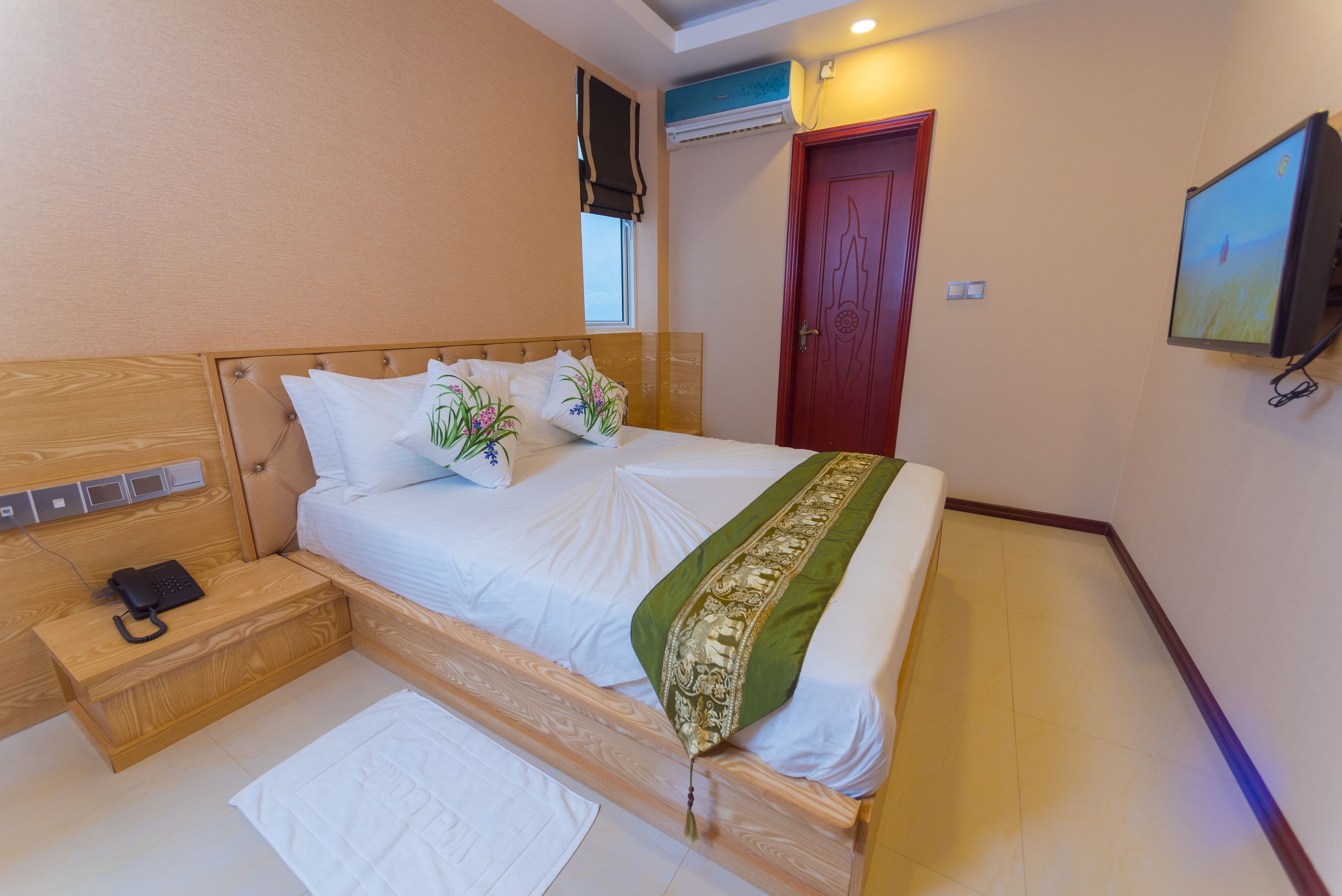 A neatly arranged bedroom with a bed, bedside table, and a television mounted on the wall.
