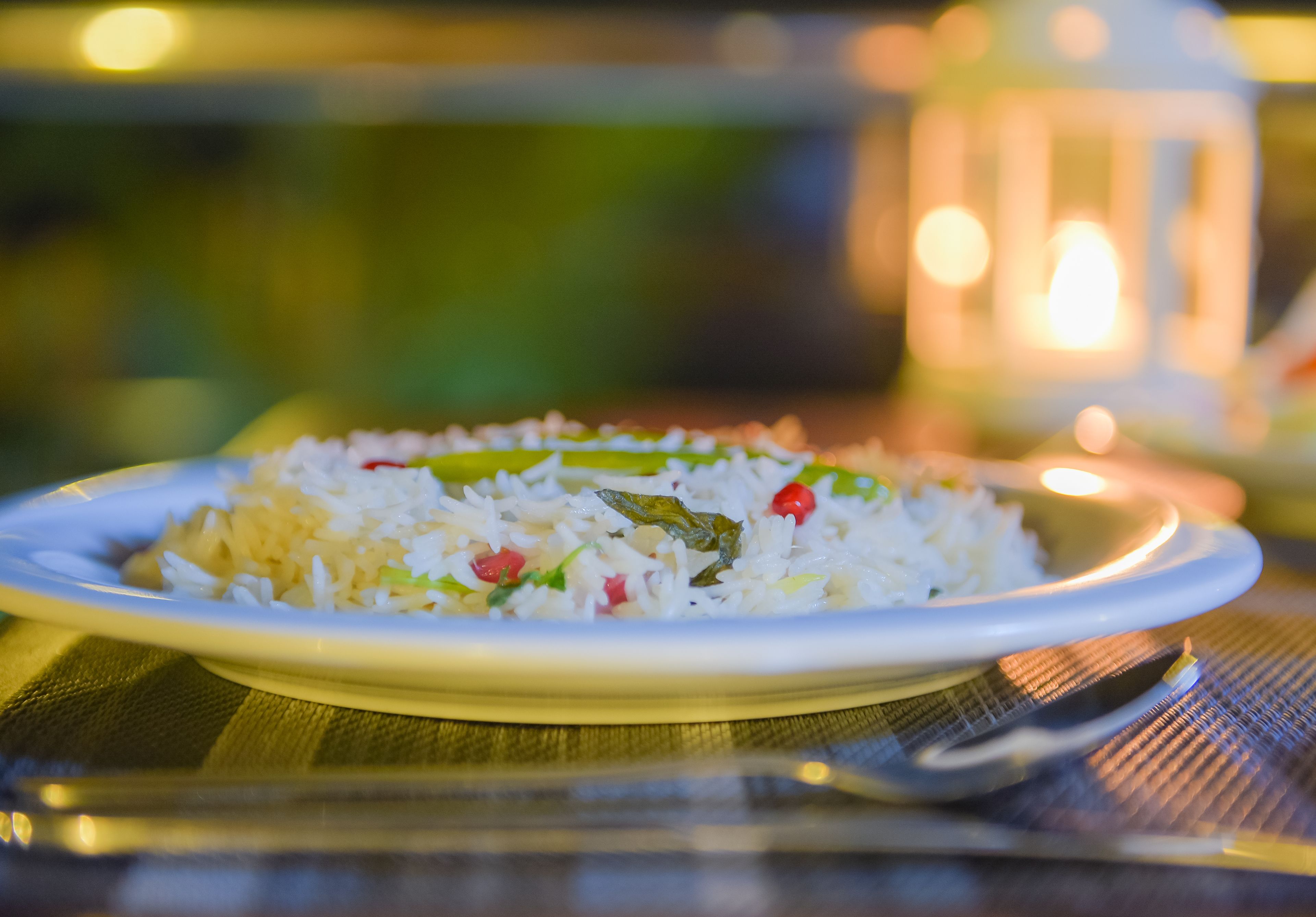 Un plato de arroz con verduras sobre una mesa, con una vela al fondo.