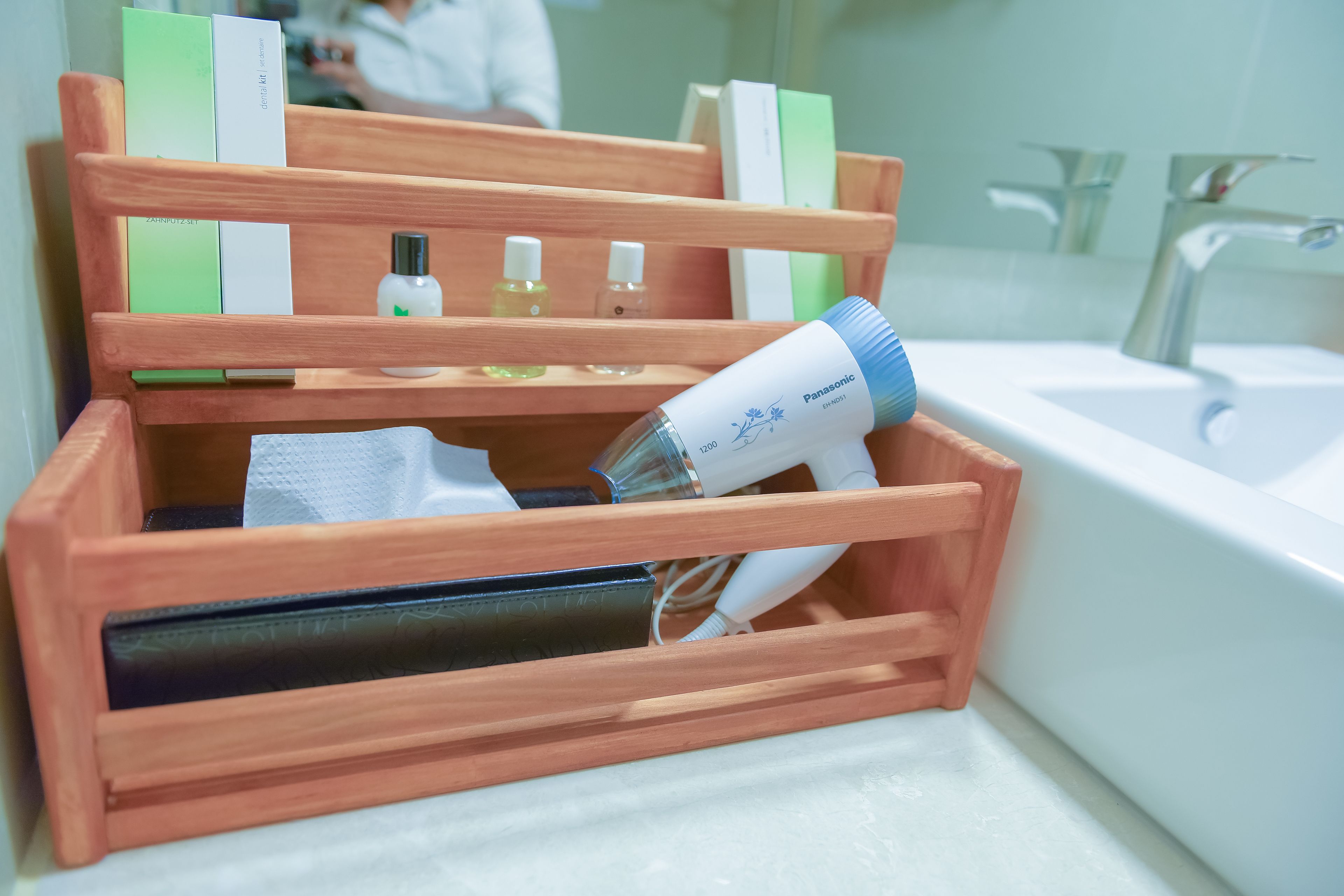 A wooden organizer with toiletries and a hairdryer on a bathroom counter.