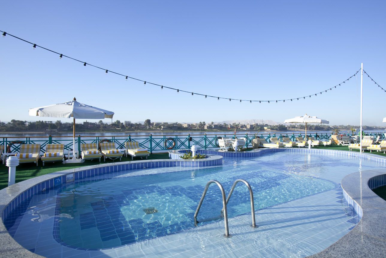 Piscina en la azotea con sillones de descanso y sombrillas, rodeada por una barandilla y luces colgantes.