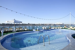 Piscina en la azotea con sillones de descanso y sombrillas, rodeada por una barandilla y luces colgantes.