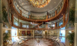 Un vaste atrium à plusieurs niveaux, doté d’une fontaine centrale, de balustrades décoratives et d’une grande fresque au plafond.