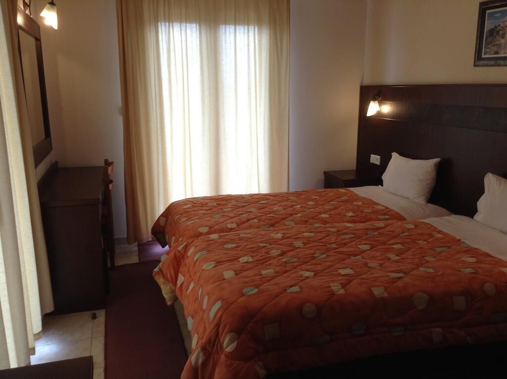 A hotel room with a large bed, a nightstand, a dresser, and a window with curtains.