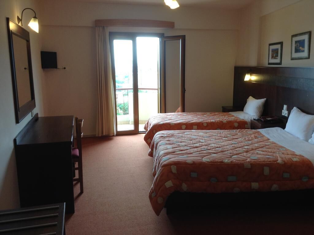 A hotel room with two beds, a desk, and a sliding door to the balcony.
