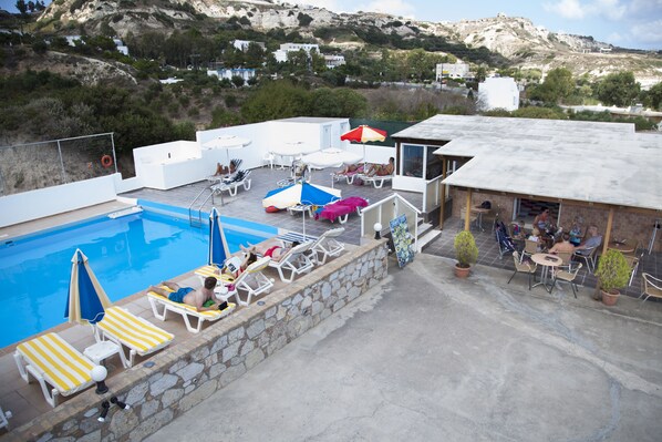 Área de piscina en la azotea con sillones, sombrillas y zona de comedor.