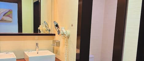 A modern bathroom with two sinks, a mirror, a hairdryer, and a toilet.