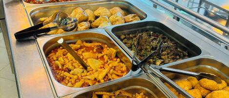 Un bufé con diversas opciones de comida, incluyendo ensaladas, carnes y alimentos fritos.