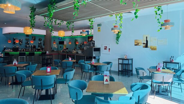 A modern restaurant interior with blue chairs, a bar area, and hanging plants. - Hotel La Cantueña (Fuenlabrada)
