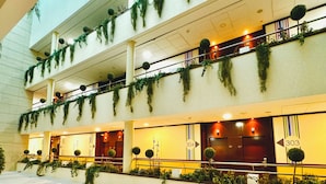 Interior de un hotel con varios niveles, balcones decorados con follaje y adornos esféricos.