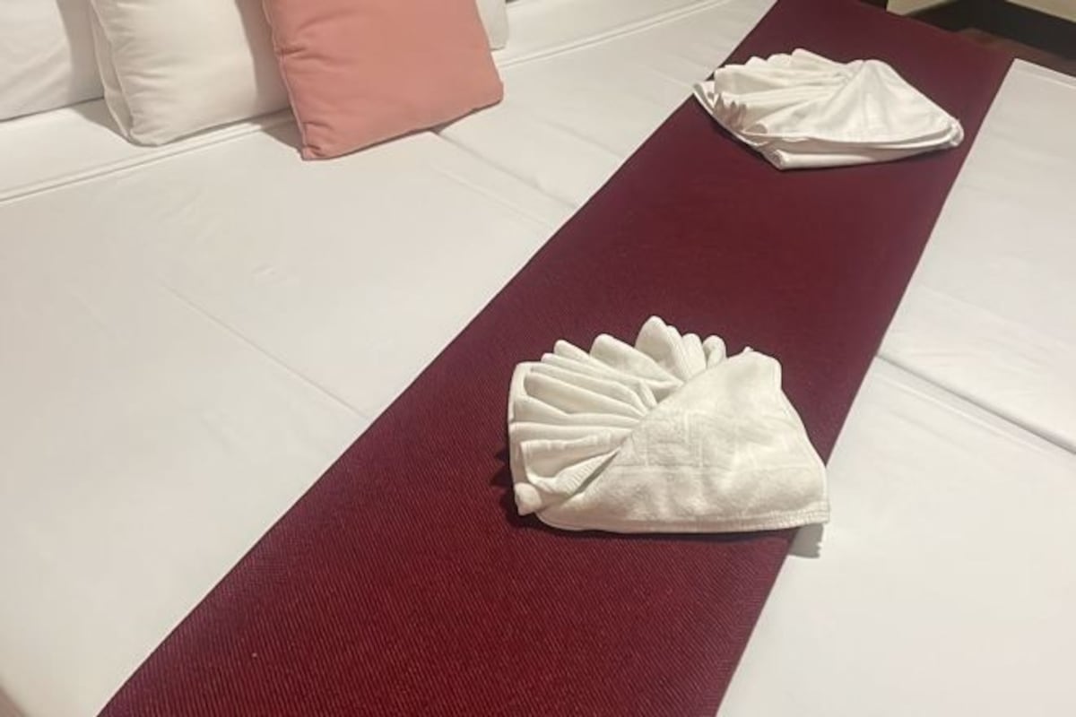 A neatly made bed with a red runner and two folded white towels.