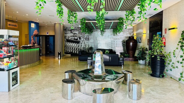 A modern lobby with a reception desk, seating area, and decorative plants. - Hotel La Cantueña (Fuenlabrada)