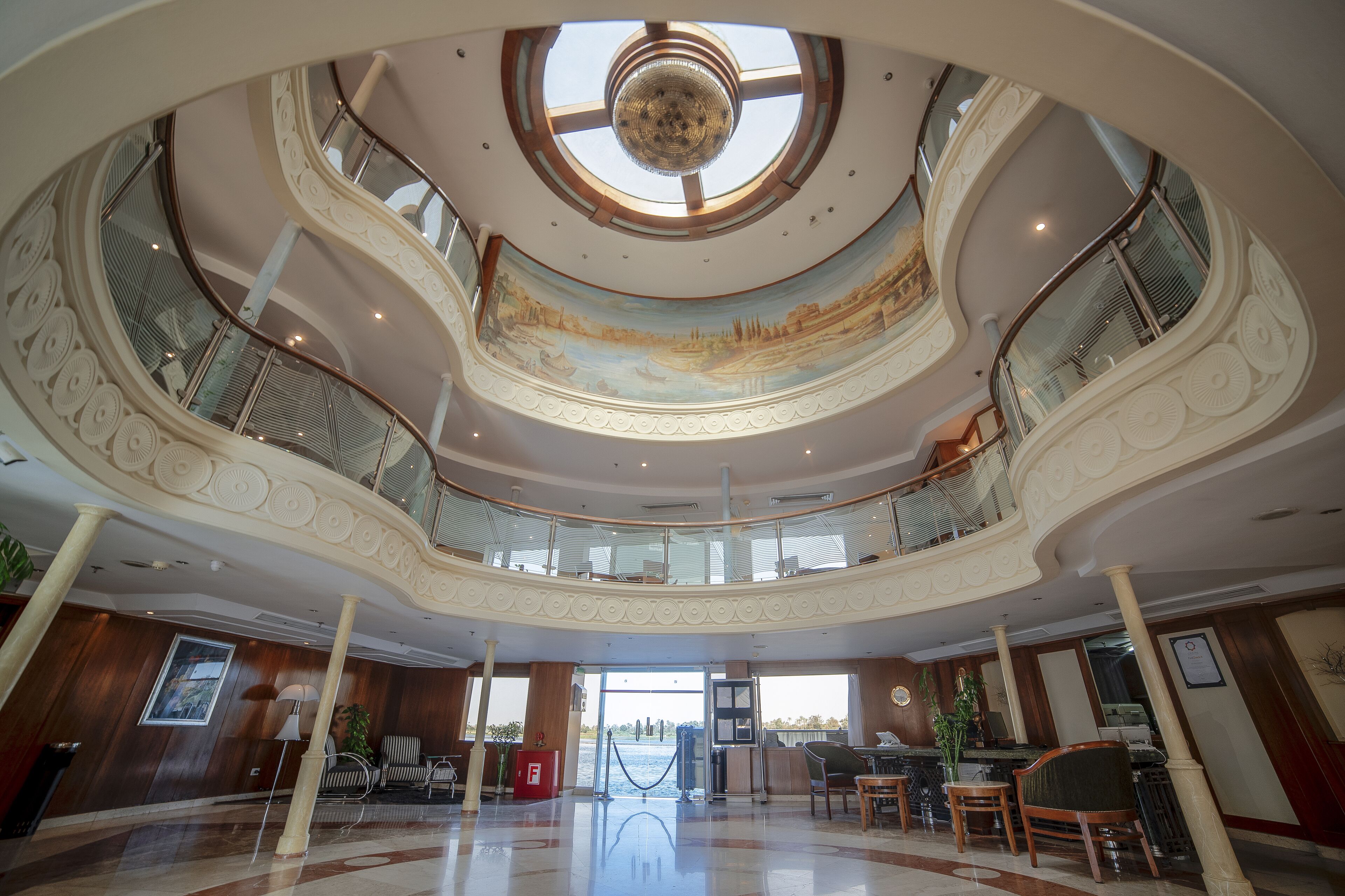 A multi-level atrium with a central skylight, a mural, and a reception desk.