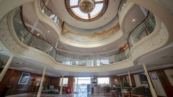 A multi-level atrium with a central skylight, a mural, and a reception desk.