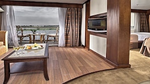 A room with a wooden floor, a sofa, a table with a bottle and glasses, a bed, and a TV. - Sonesta Star Goddess Nile cruise ship - 4 & 7 nights - From Luxor every Saturday (Luxor)