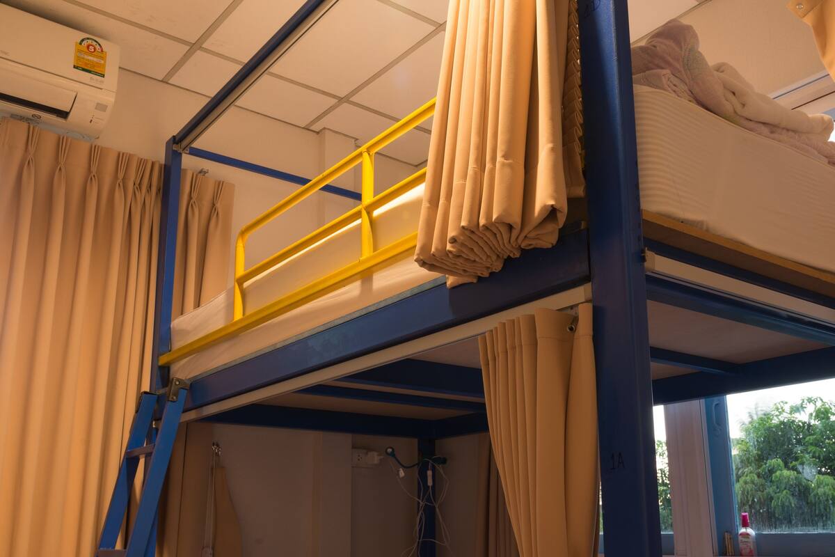 Ein Schlafraum mit Etagenbett, einer Leiter, Vorhängen und einem Fenster mit Blick auf Bäume.