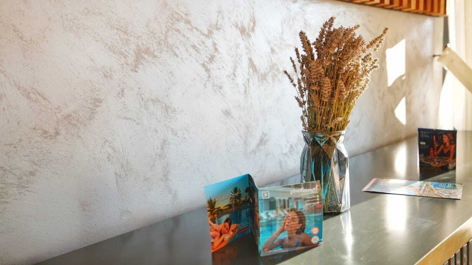 A table with a vase of dried flowers, a postcard, and a magazine.