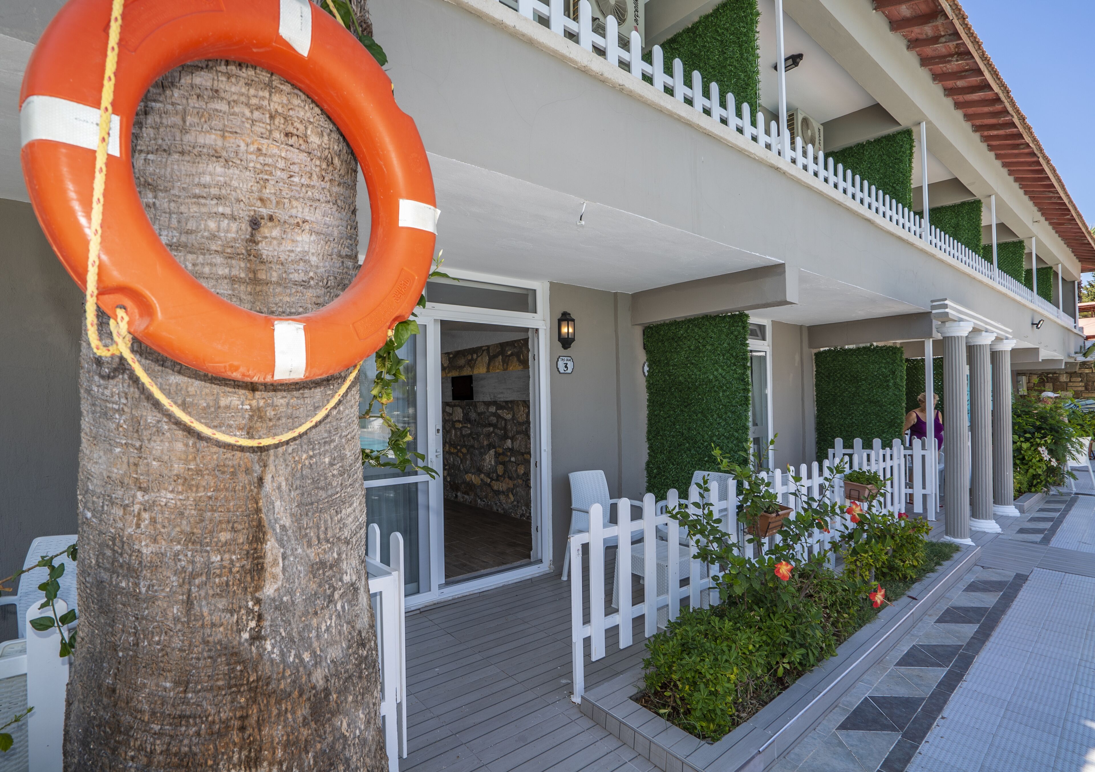 A building with a white picket fence, a wooden deck, and a lifebuoy hanging from a tree.