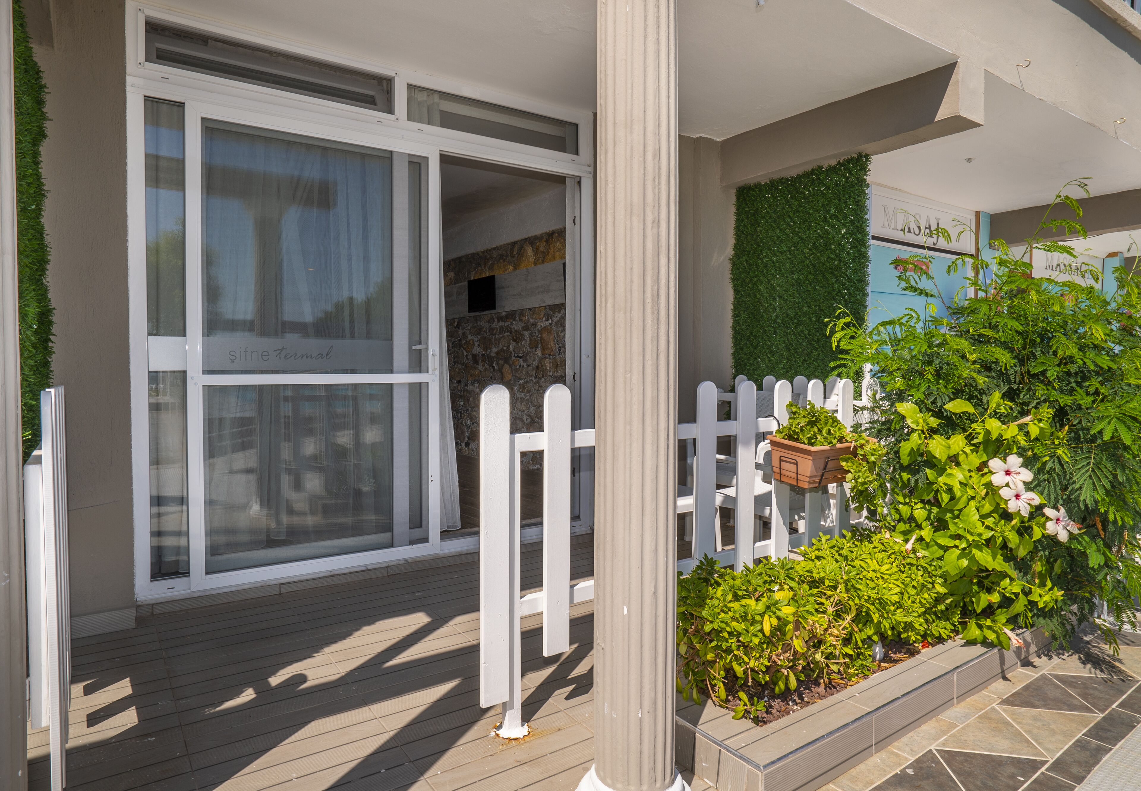 A modern building with large glass windows, a wooden deck, and a white picket fence.