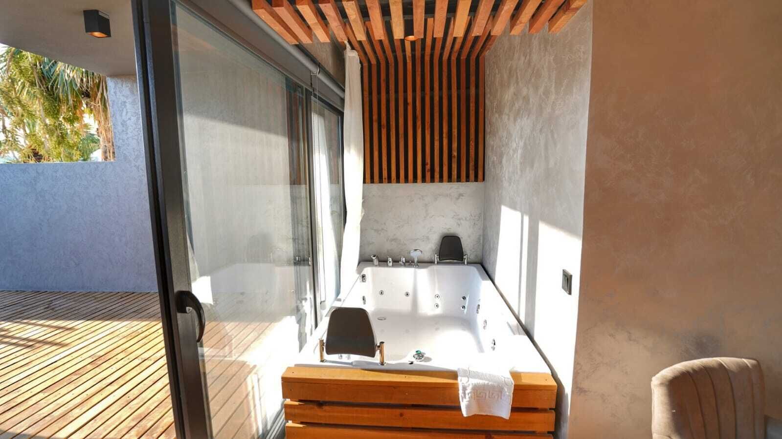A modern outdoor spa area with a wooden deck, a large hot tub, and a glass door leading to a patio.