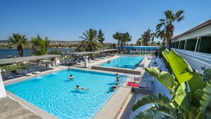 A swimming pool with multiple lanes, surrounded by lounge chairs and palm trees, overlooking a body of water. - Sifne Thermal Otel (Cesme)