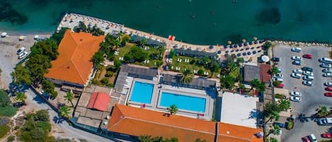 Vista aérea de un resort con piscina, estacionamiento y acceso a la playa.