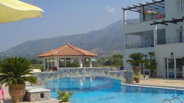A swimming pool with a tiled deck, a covered gazebo, and a building with balconies. - Pinelopi Apartments (Apokoronas)
