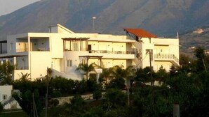A multi-story building with balconies, surrounded by greenery and mountains in the background. - Pinelopi Apartments (Apokoronas)