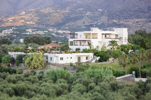 Un edificio residencial de varios pisos con balcones, rodeado de vegetación y un paisaje montañoso.