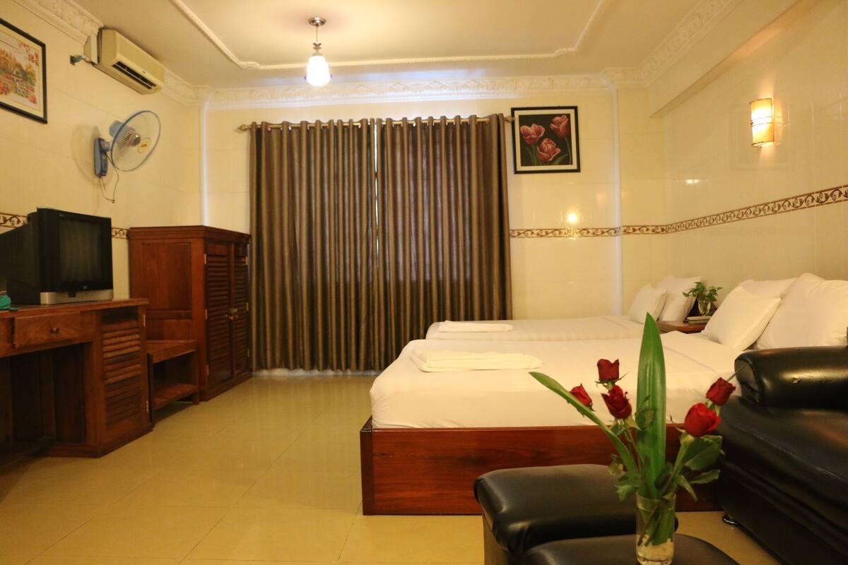 A hotel room with a bed, a desk with a television, a chair, and a vase with flowers.