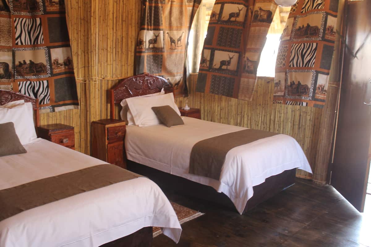 Habitación con dos camas, cabeceros de madera y una pared decorada con colchas de motivos animales.