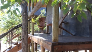 Eine Holzdielen-Terrasse mit schlichtem Geländer, einem Blumentopf und einem Steingebäude.