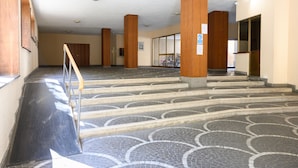 Um interior espaçoso com uma escadaria central, colunas de madeira e piso de azulejos.