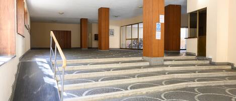 A spacious interior with a central staircase, wooden columns, and a tiled floor.