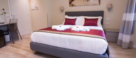 A neatly made bed with white and red linens, a desk with a chair, and a painting on the wall.