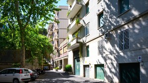 Uma rua estreita flanqueada por edifícios altos, alguns com varandas e vegetação.