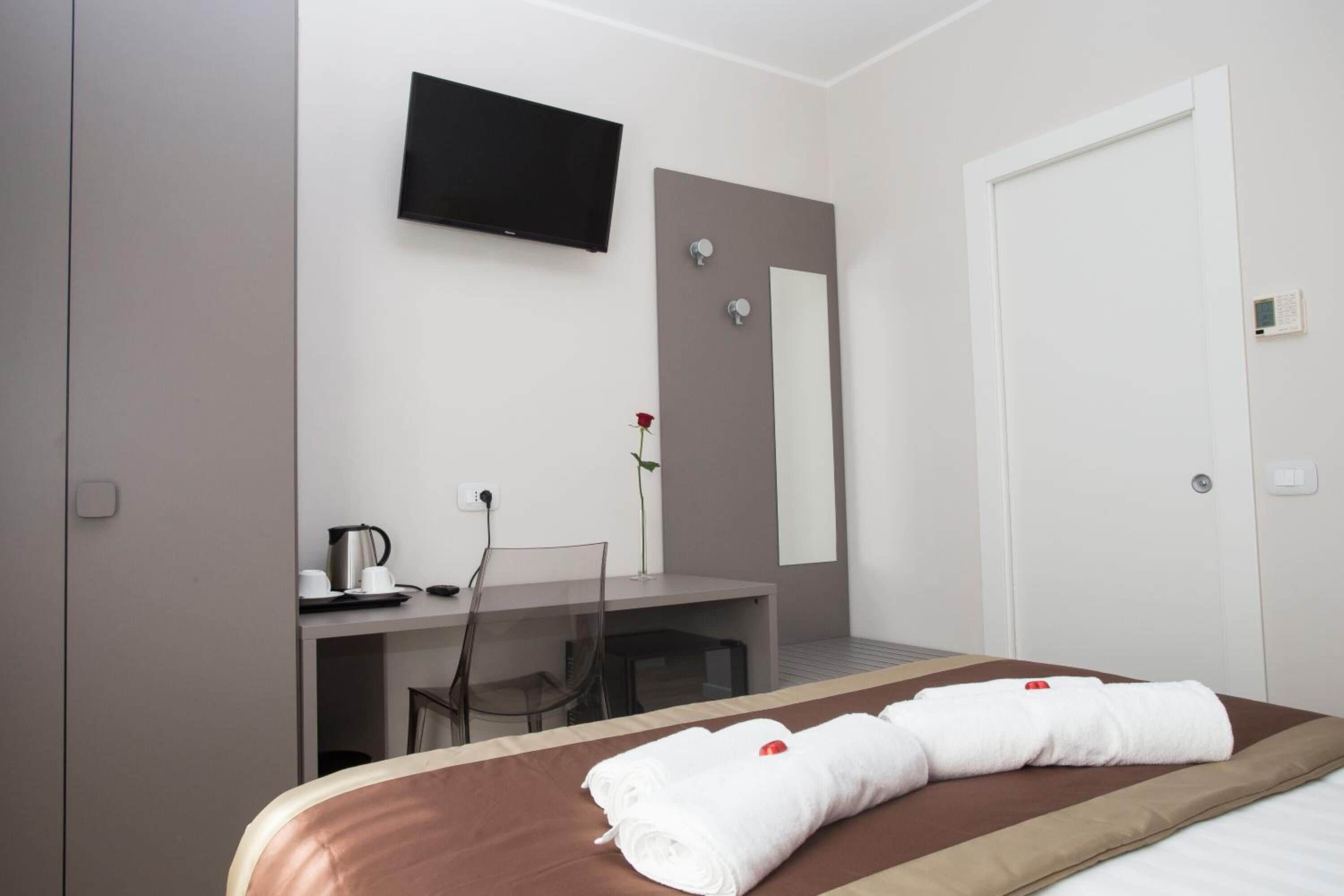 A hotel room with a bed, a desk, a chair, a television, and a mirror.
