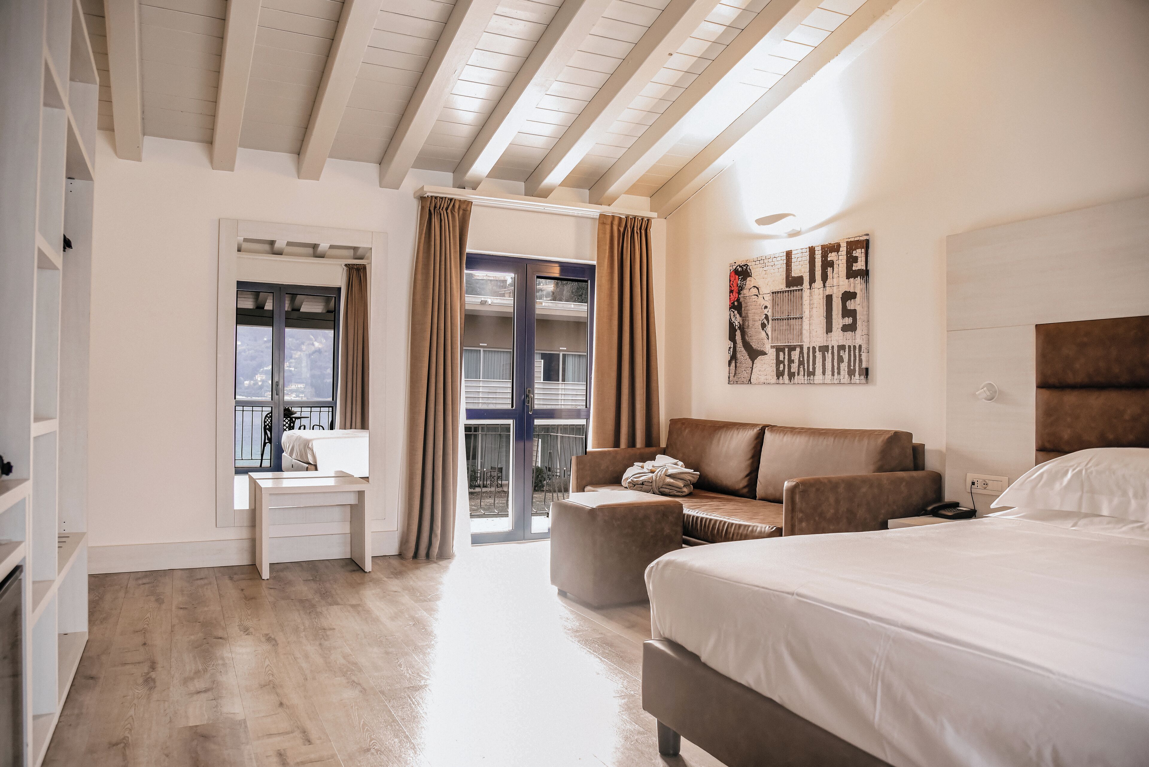 A hotel room with a bed, a sofa, a desk, and a view of the outside.