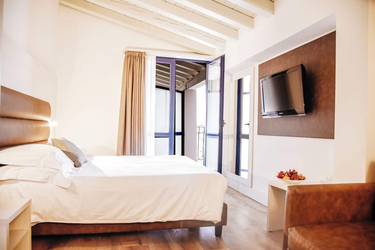 A modern bedroom with a large bed, a TV mounted on the wall, and a view of the outdoors through a glass door.