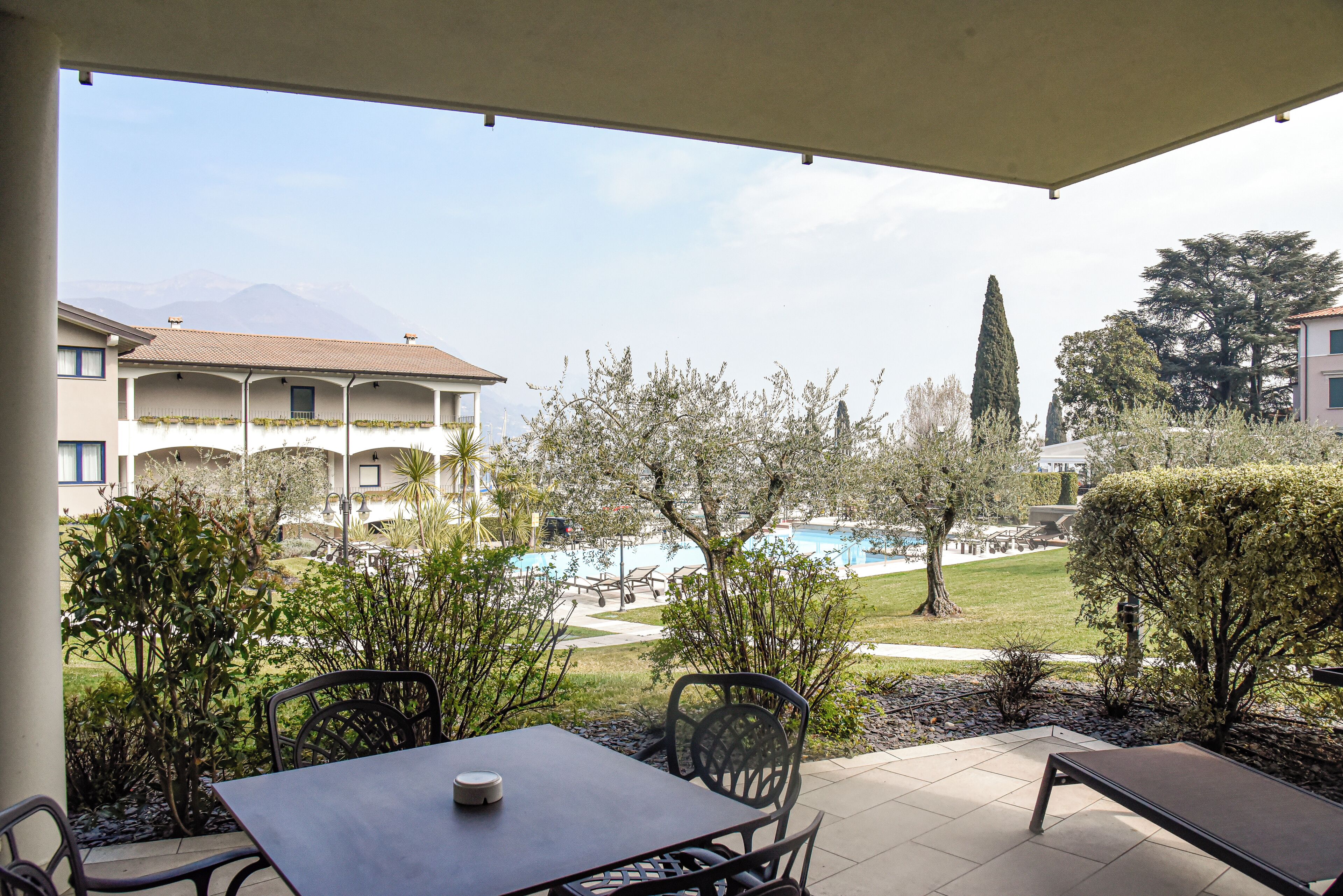 A patio with a table and chairs, overlooking a pool and a building with a tiled roof.