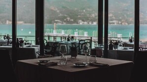 Un restaurante con vistas al mar y a las colinas. Las mesas están preparadas con copas de vino y platos.