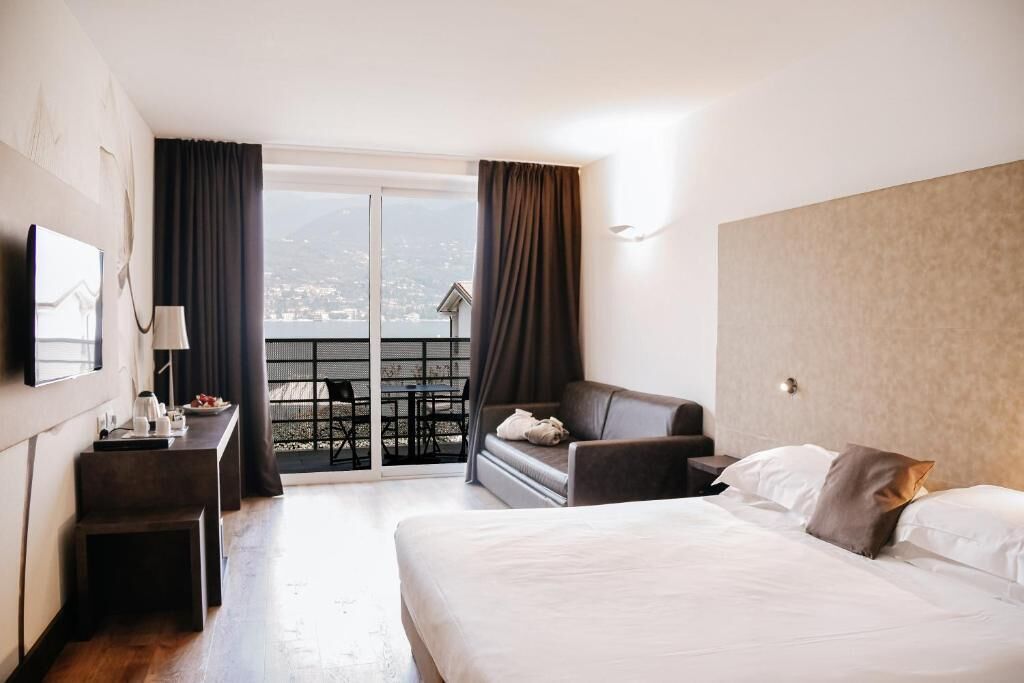 A hotel room with a bed, a desk, a chair, and a balcony with a view.