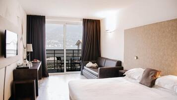 A hotel room with a bed, a desk, a chair, and a balcony with a view.