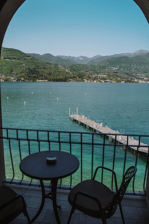 Un balcón con mesa y sillas que da a un lago con un muelle y montañas al fondo.