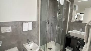 A modern bathroom with a glass-enclosed shower, a bidet, a toilet, and a sink.