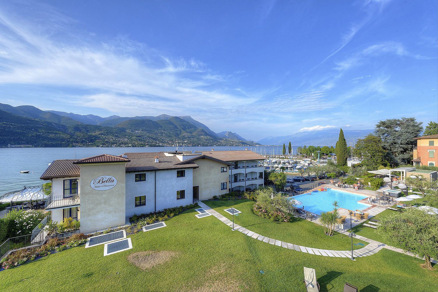 Un hotel con piscina, rodeado de césped cuidado y vistas a un lago y montañas.
