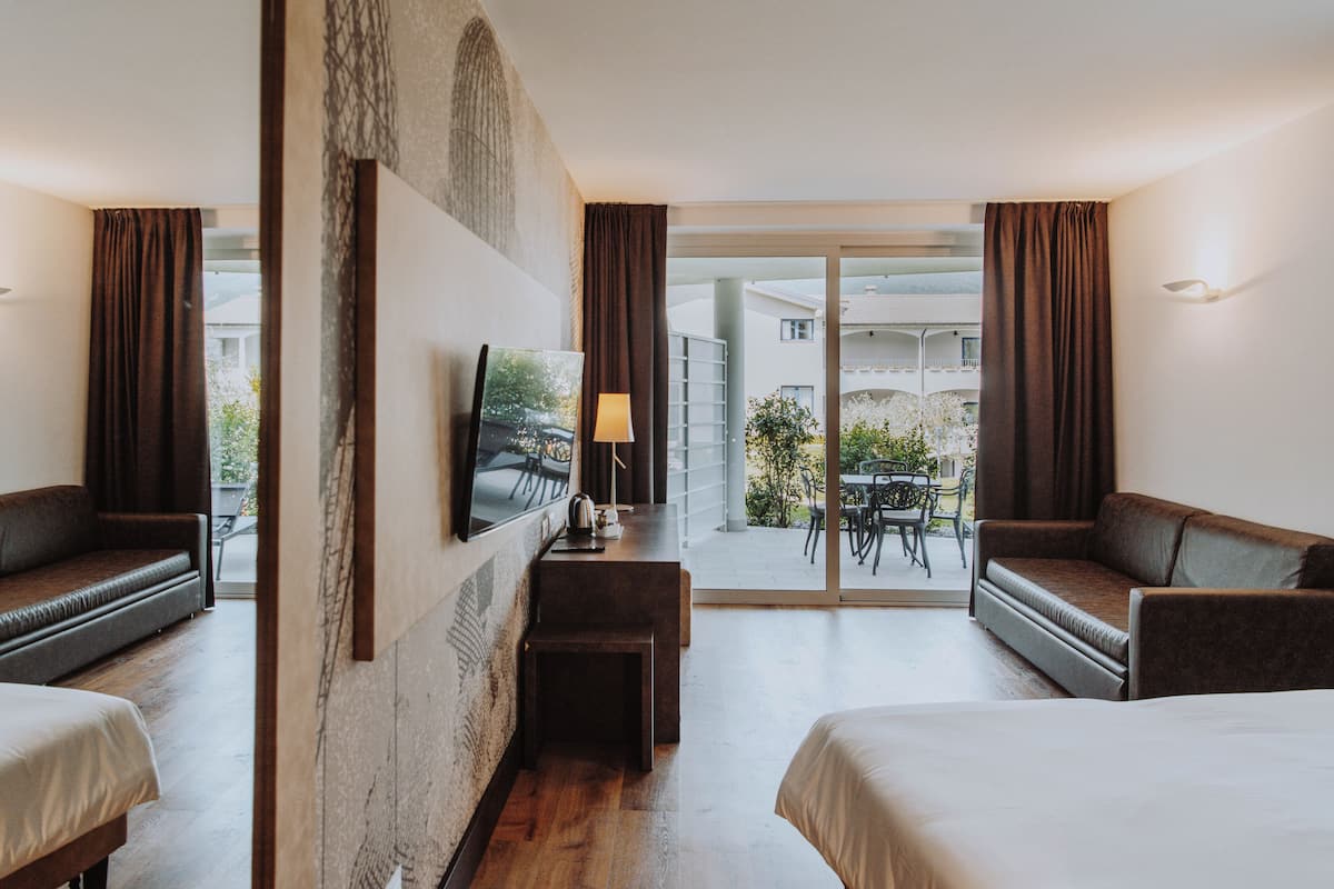 A hotel room with two beds, a desk, a TV, and a balcony with a table and chairs.
